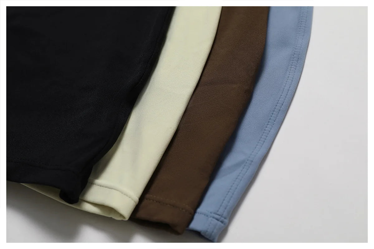 Four folded shirts in black, beige, brown, and blue on a white background