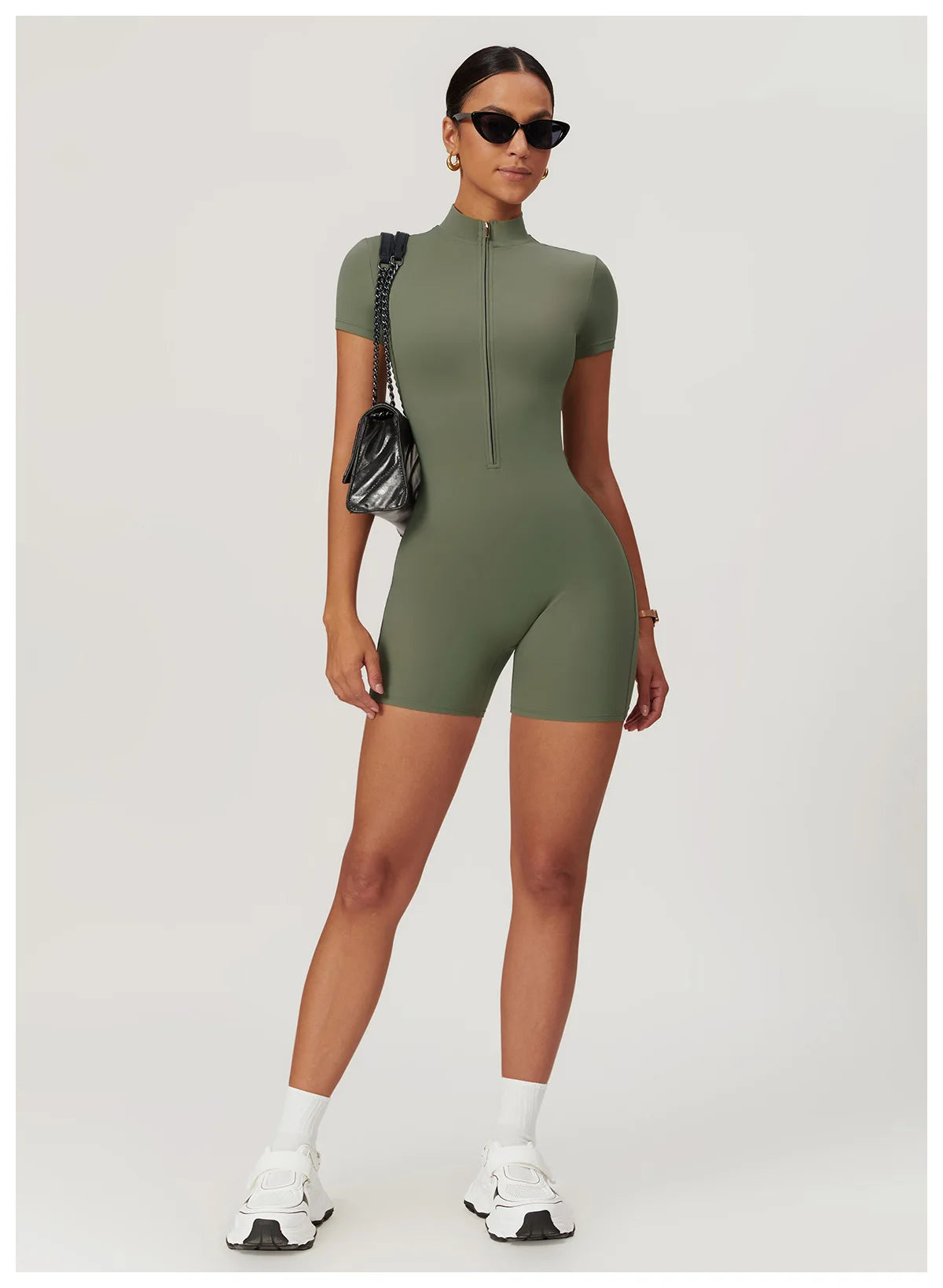 Woman wearing a green bodysuit with white sneakers on a light gray background