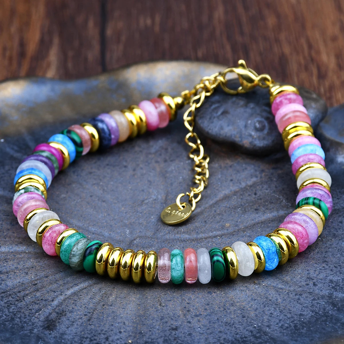 Multicolored beaded bracelet with gold accents on a stone surface