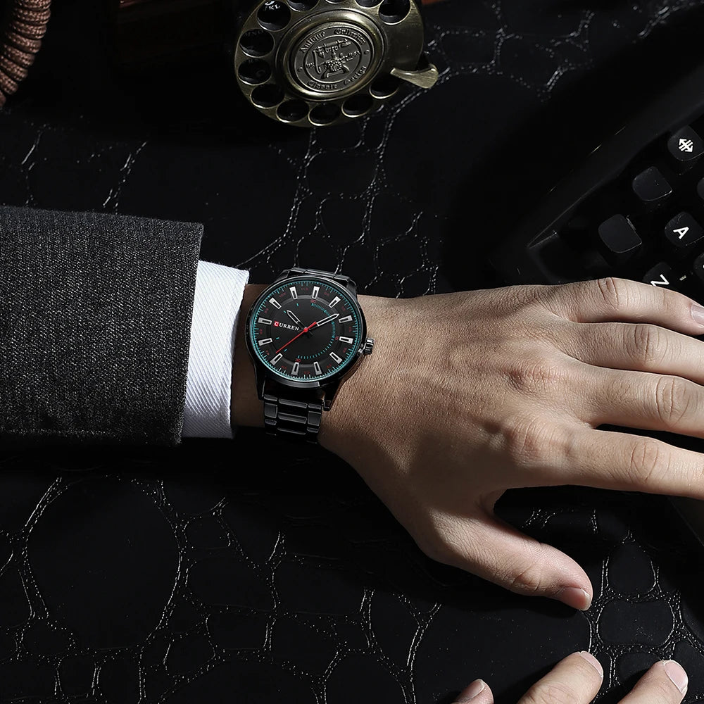 Hand wearing a black wristwatch on a dark surface with a vintage phone and keyboard.