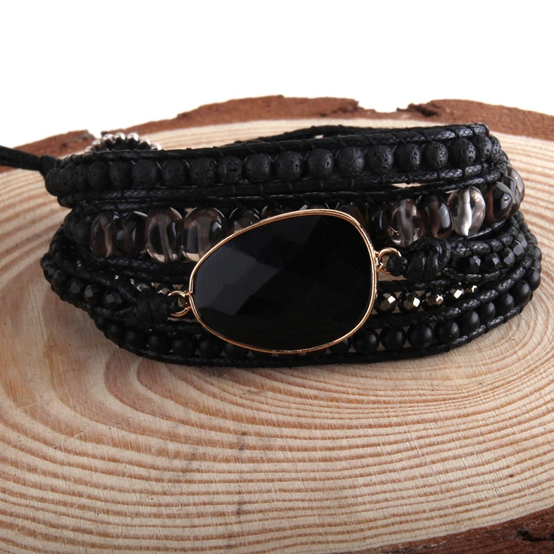 Black beaded bracelet with a large black stone and gold accents on a wooden surface