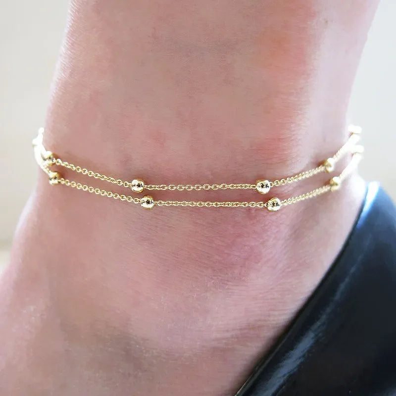 Gold anklets on a person's ankle against a neutral background