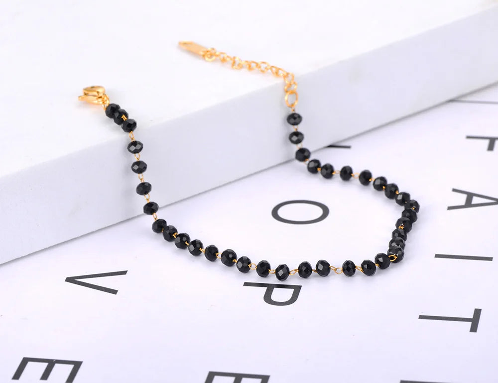 Black beaded necklace with gold clasp on a white surface with black lettering