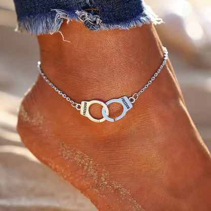 Ankle bracelet with handcuff design and 'FREEDOM' on a person's ankle against a blurred background.
