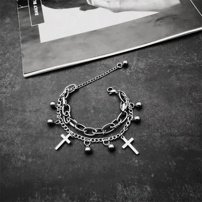 Stack of silver chain bracelets with cross charms on a dark surface.