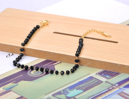 Black beaded bracelet with gold clasp on a wooden surface