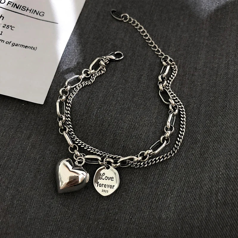 Silver chain bracelet with heart and 'Love forever' charm on a dark surface