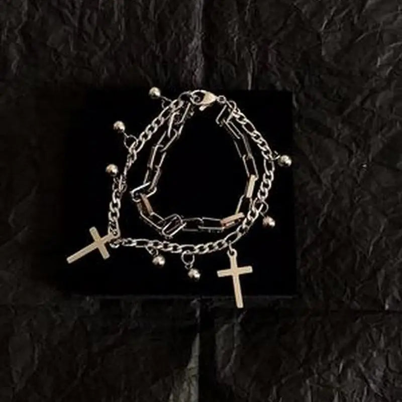 Stack of silver chain bracelets with cross pendants on a black textured background
