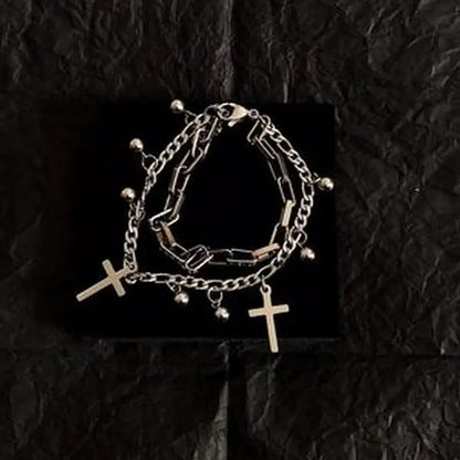 Stack of silver chain bracelets with cross pendants on a black textured background
