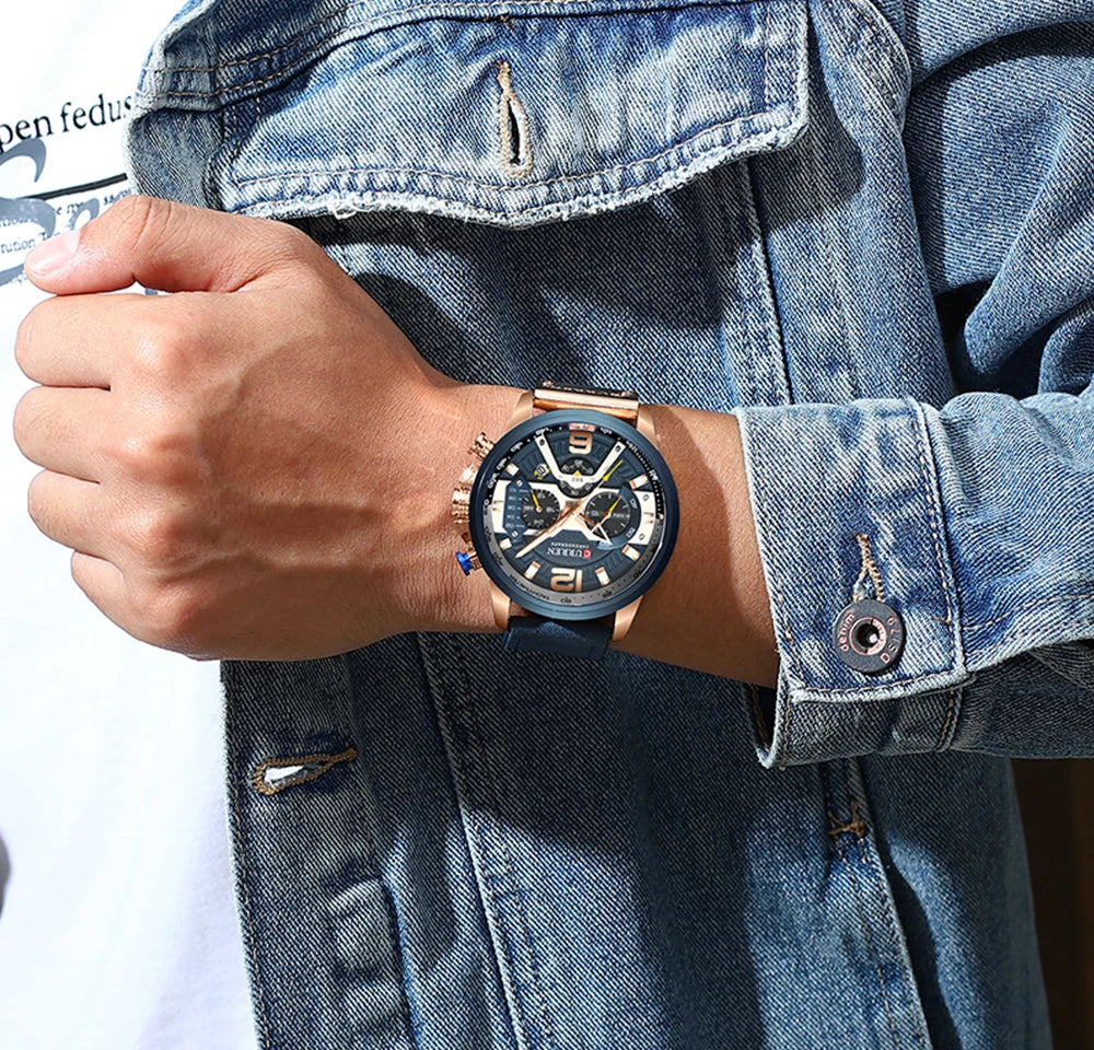 Person wearing a watch with a blue face and rose gold case, against a denim jacket background.