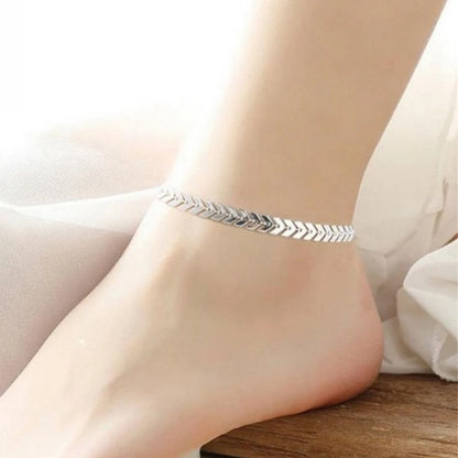 Silver anklet on a person's ankle against a neutral background