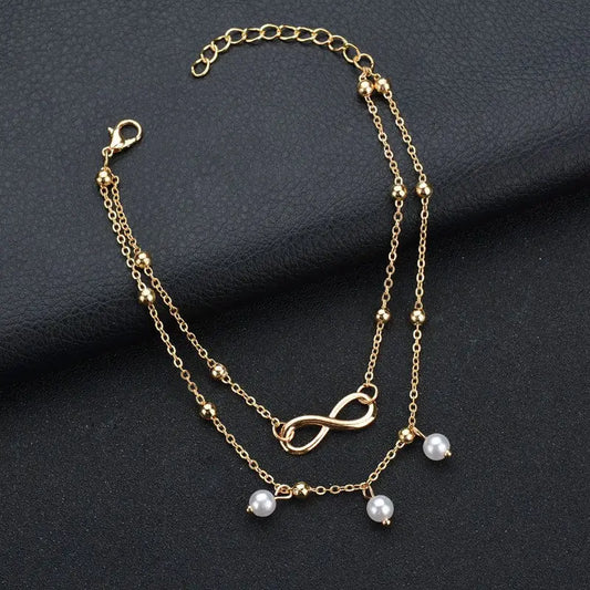 Gold bracelet with infinity symbol and pearl charms on a dark background