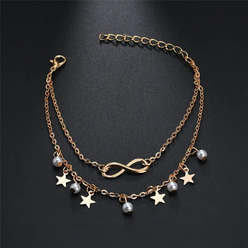 Gold chain necklace with star and pearl charms on a black background