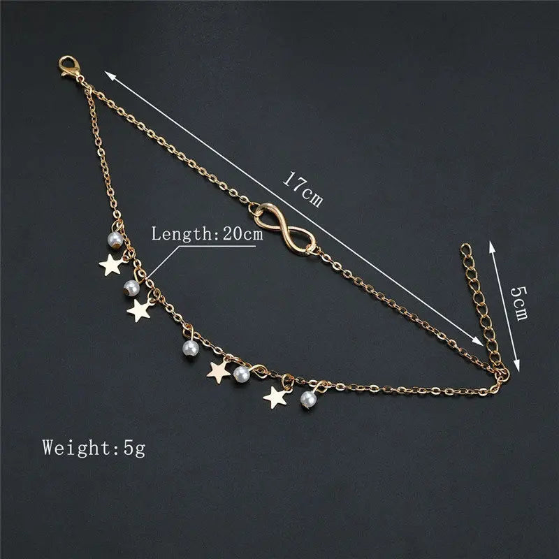 Gold anklet with star and pearl charms on a dark background, showing measurements.