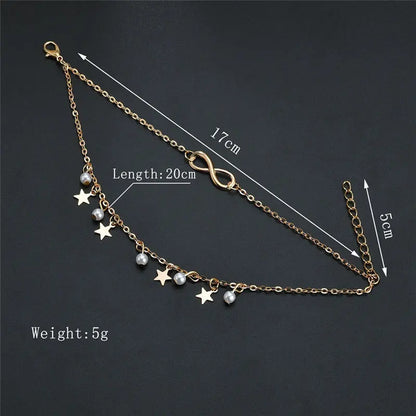 Gold anklet with star and pearl charms on a dark background, showing measurements.