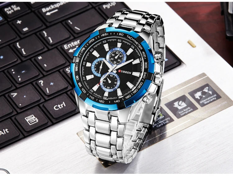 Silver watch with a black and blue face on a white surface with a keyboard in the background