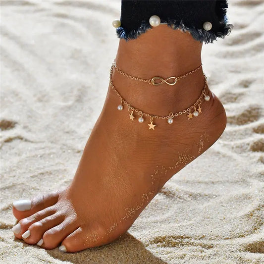 Ankle with gold anklets featuring pearls and star charms on a sandy background