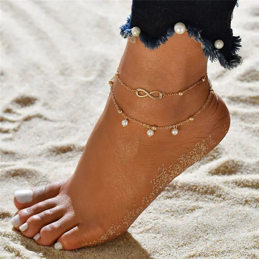 Anchored foot with gold anklets and pearls on a sandy background