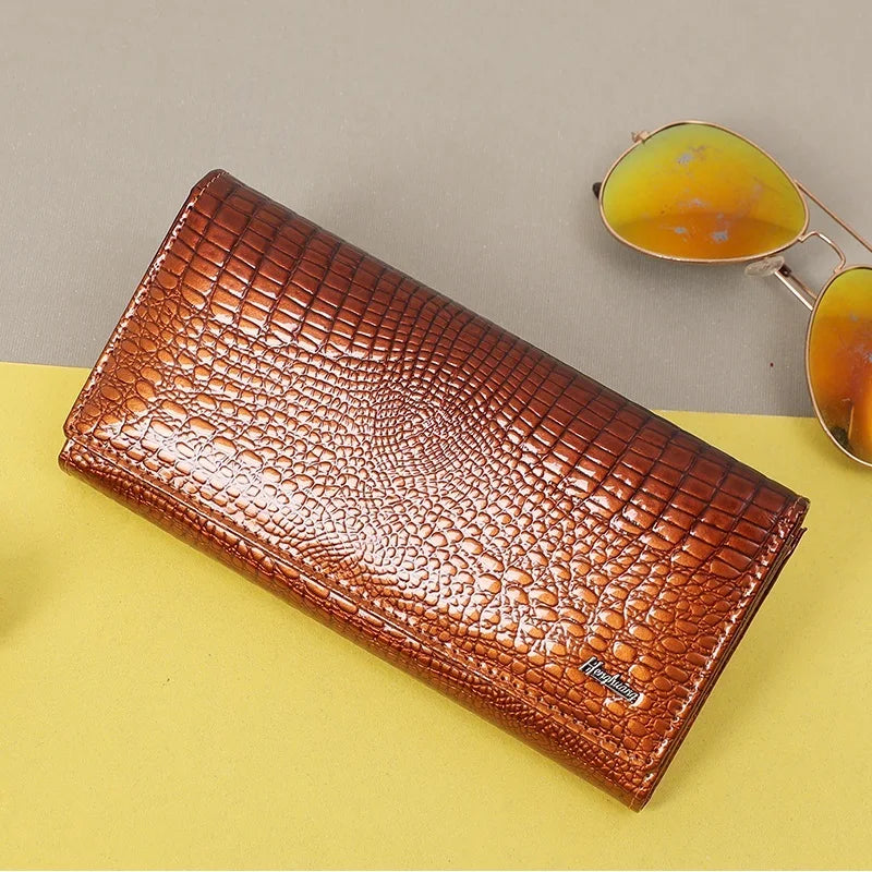 Brown crocodile-patterned wallet on a yellow surface with sunglasses in the background