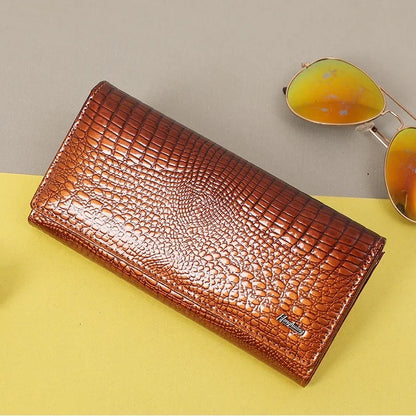 Brown crocodile-patterned wallet on a yellow surface with sunglasses in the background
