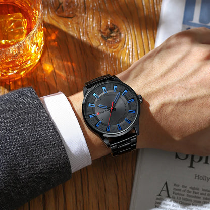 Person wearing a black wristwatch with blue accents on a wooden table with a glass of whiskey.