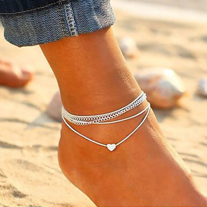 Ankle bracelet with heart charm on a foot against a beach background