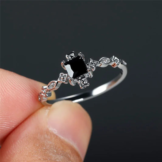 Silver ring with a black gemstone held between fingers against a dark background