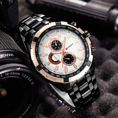 Luxury watch with black and rose gold design on a textured surface with camera lens in the background