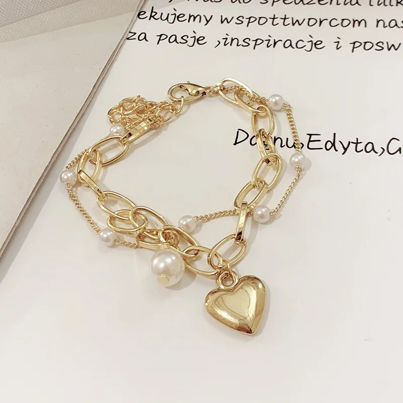 Gold bracelet with heart charm and pearls on a light background