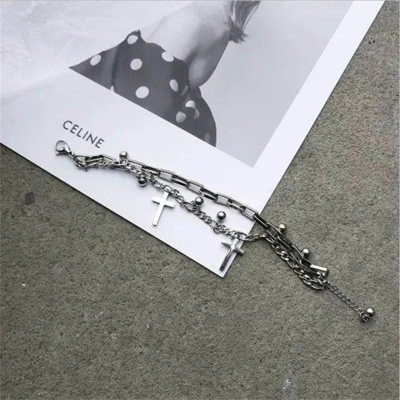 Silver chain bracelet with cross charms on a gray surface with a Celine magazine in the background.