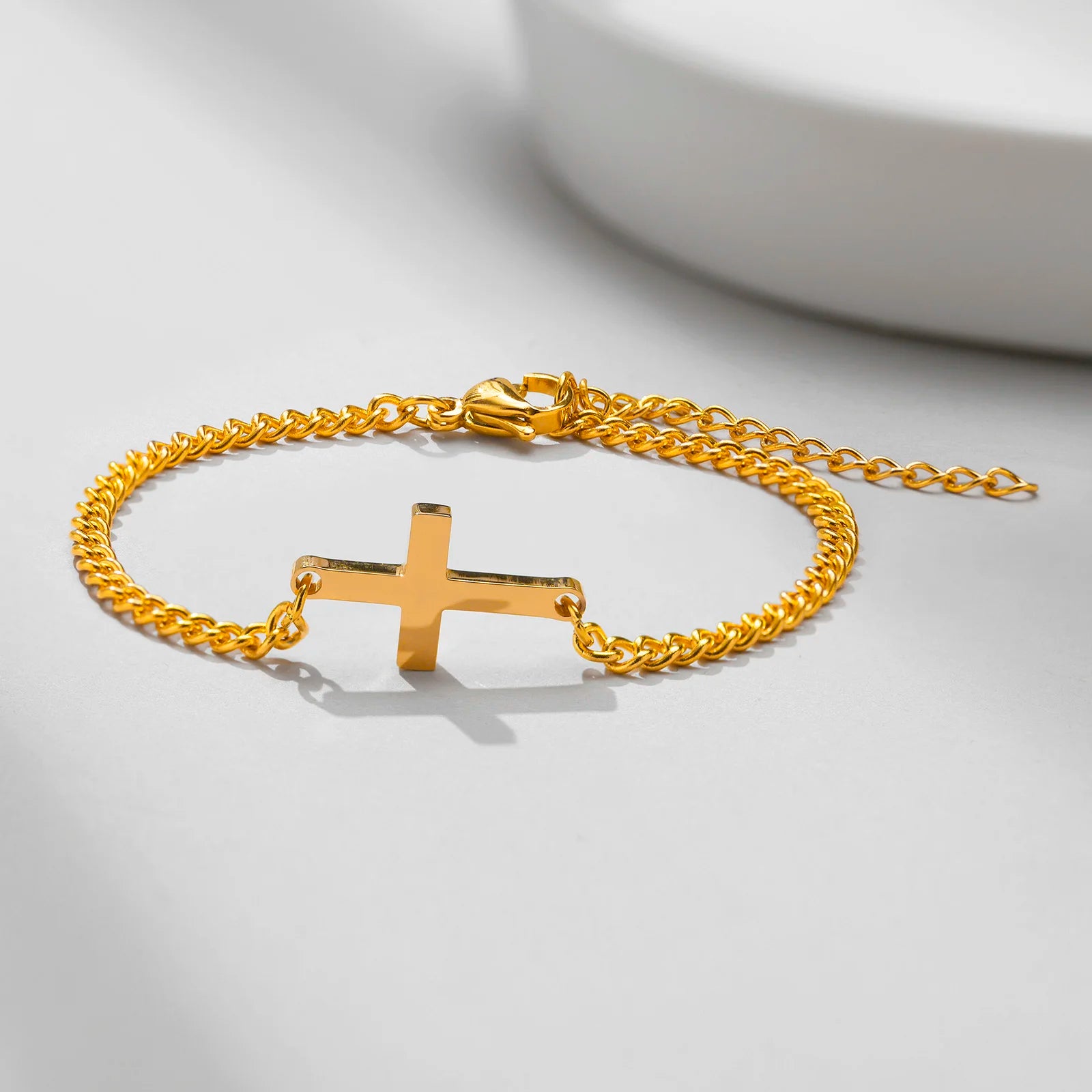 Gold bracelet with a cross pendant on a light gray background