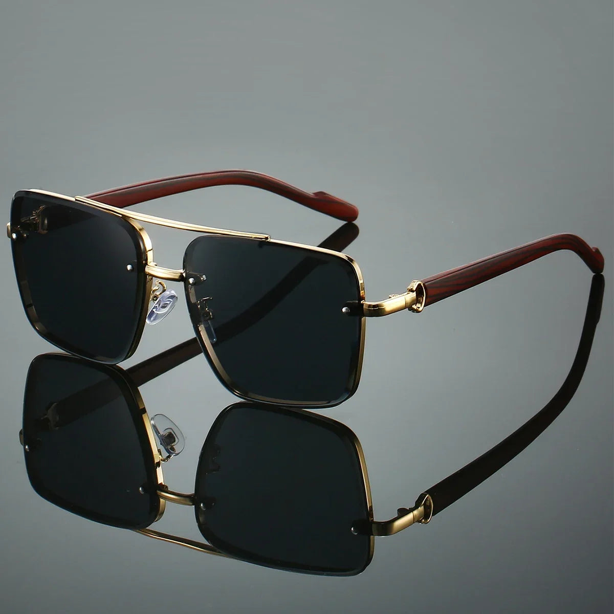 Sunglasses with gold frames and dark lenses on a reflective surface with a gray background