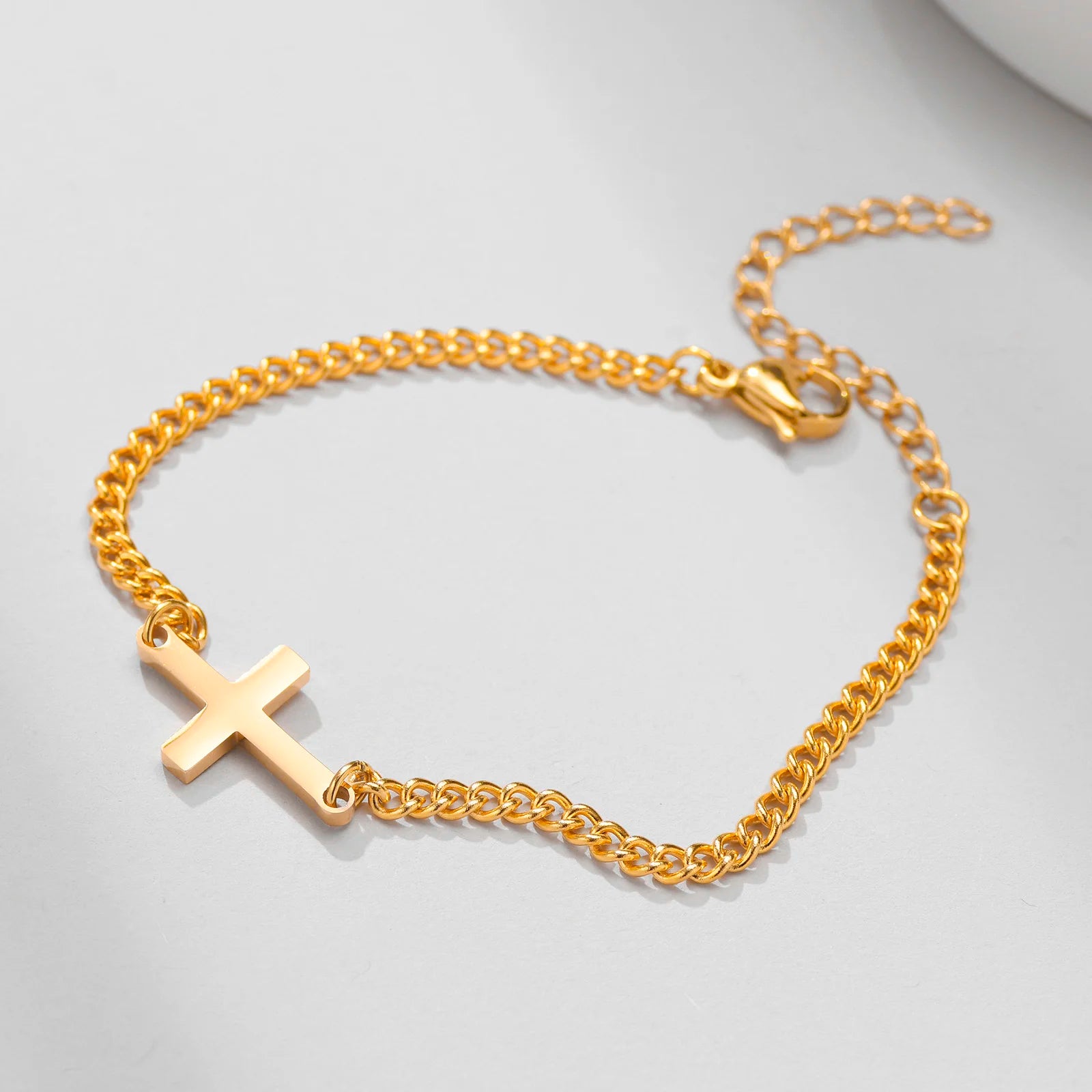 Gold chain bracelet with a cross pendant on a light gray background
