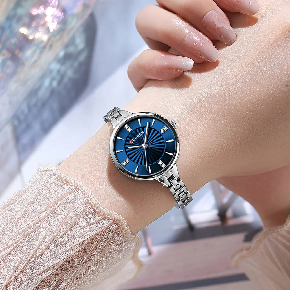 Wristwatch with blue dial and silver case on a wrist, blurred background
