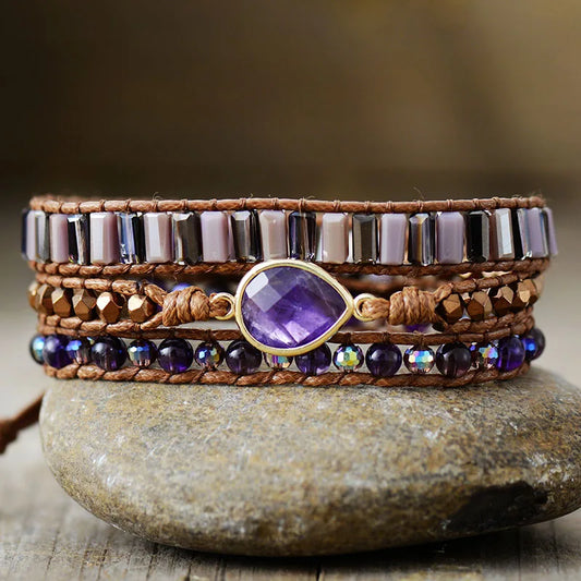 Multistrand beaded bracelet with a purple gemstone on a stone surface