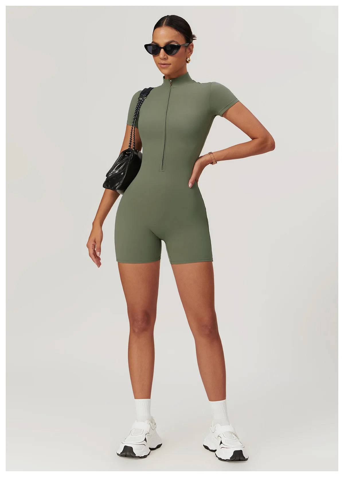 Woman wearing a green bodysuit with sunglasses and a black handbag on a white background