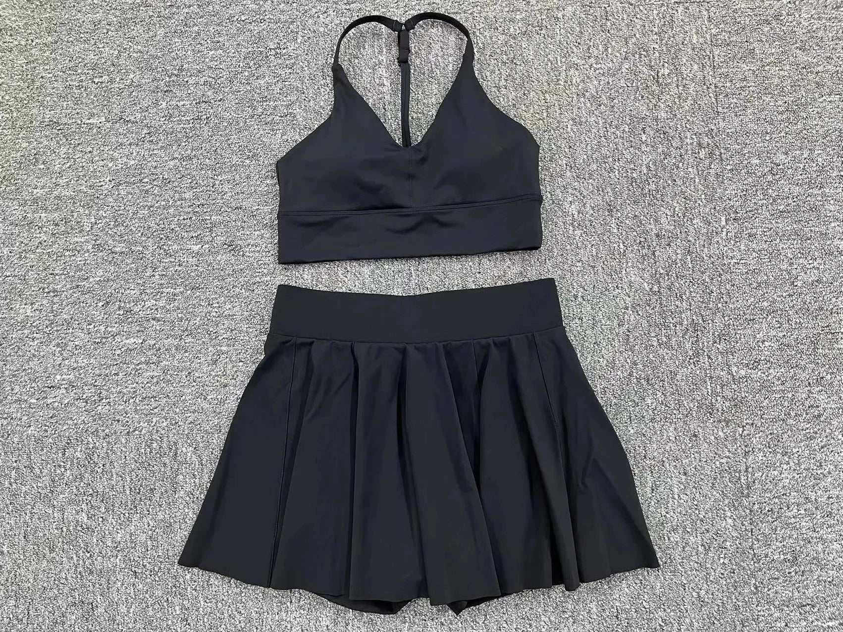 Black sports bra and skirt set on a textured gray surface