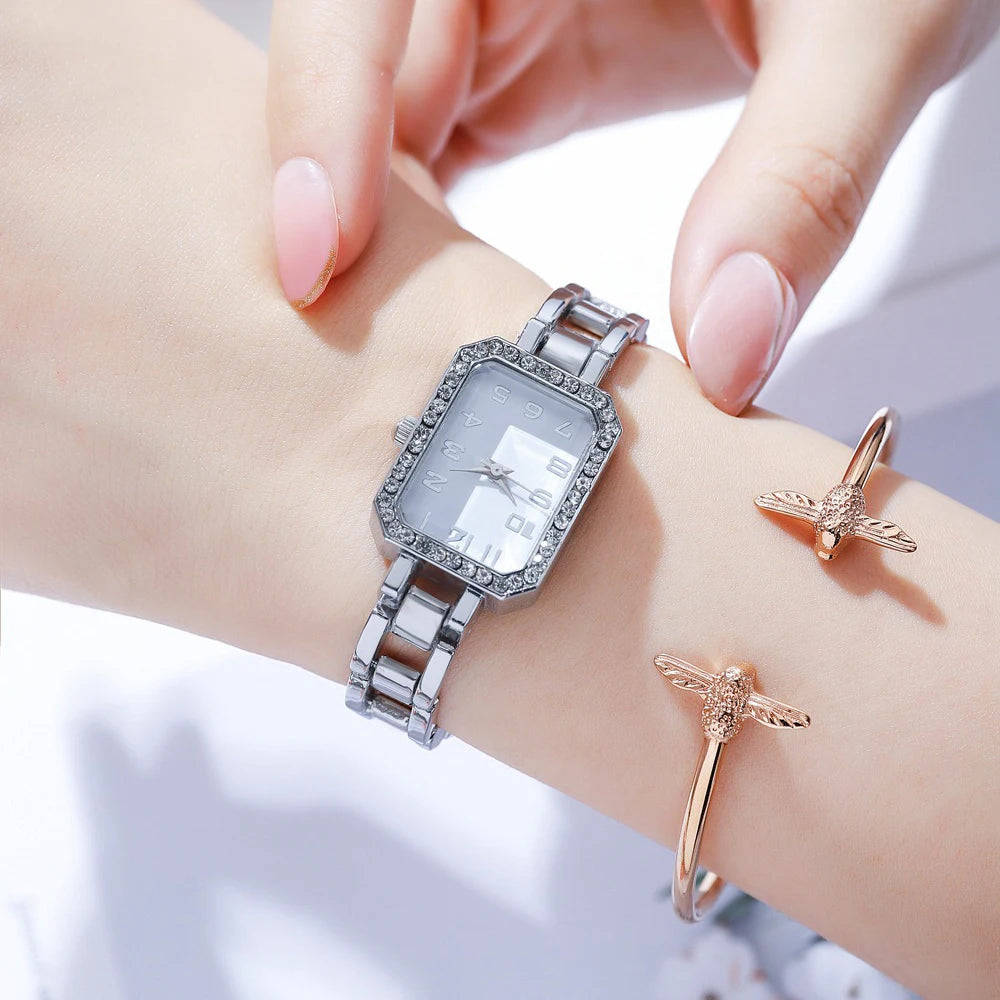 Silver watch and rose gold rings on a wrist against a light background