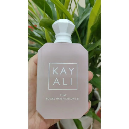 Hand holding a bottle of KAY ALI perfume with green plants in the background