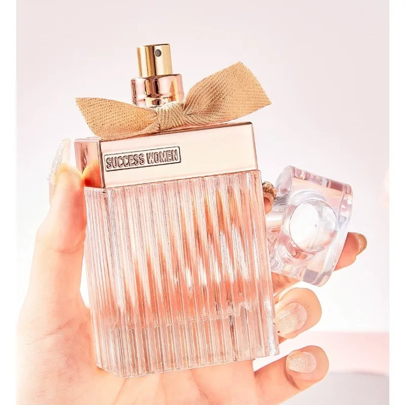 Perfume bottle with gold bow held by a hand on a light background