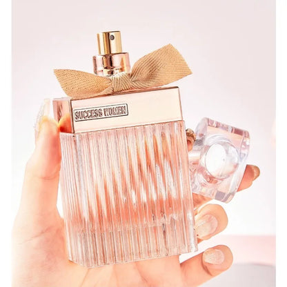 Perfume bottle with gold bow held by a hand on a light background