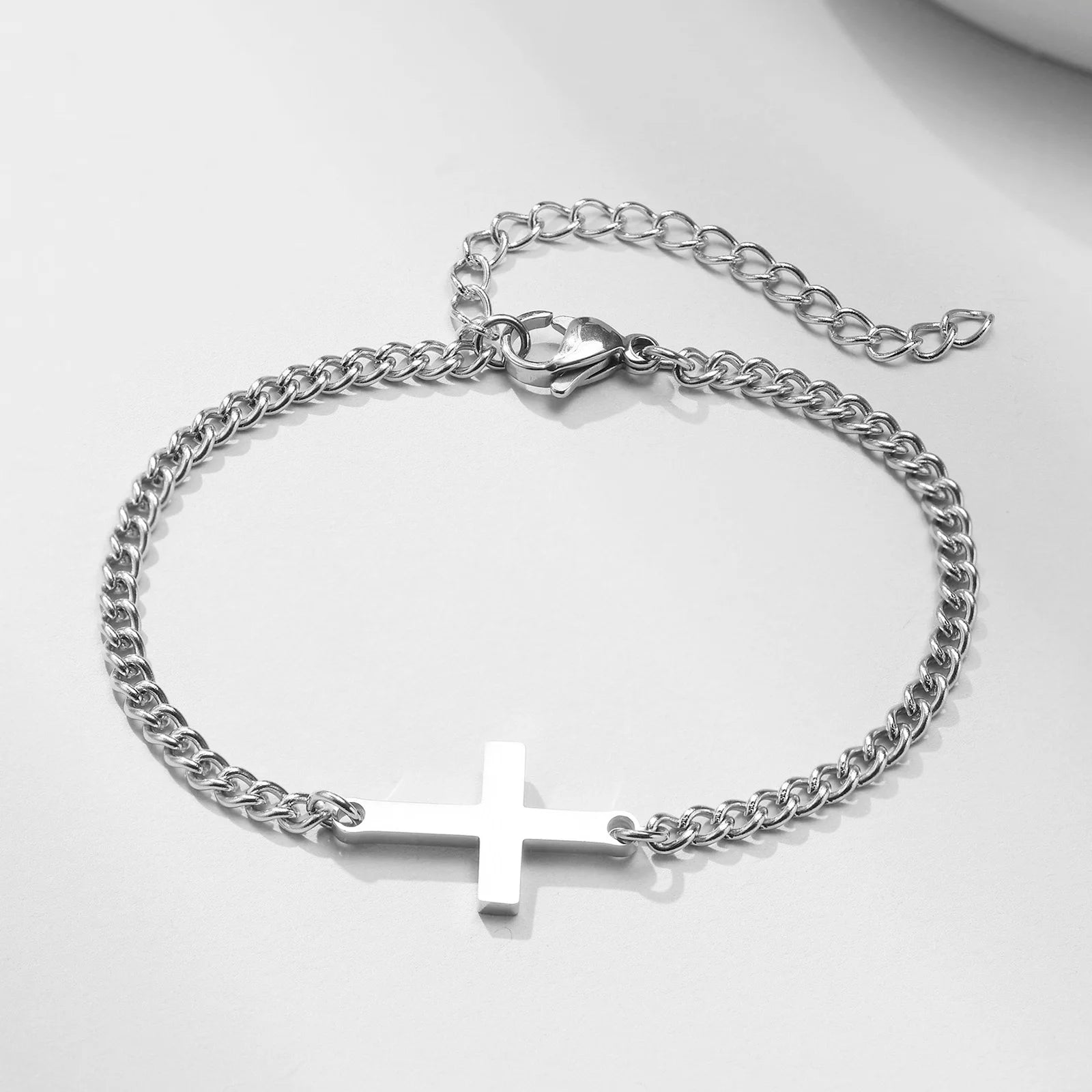 Silver chain bracelet with a cross pendant on a light gray background