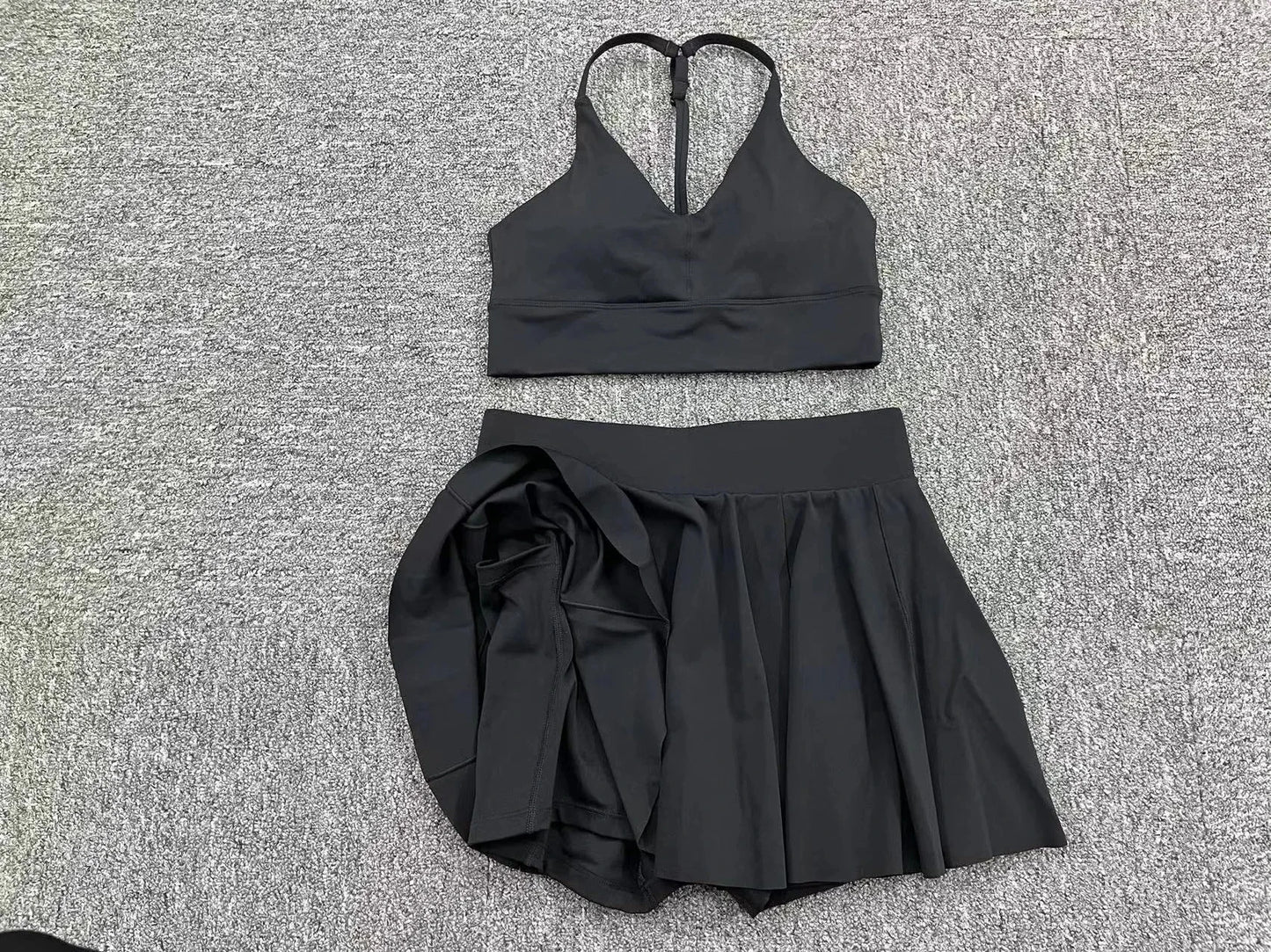 Black sports bra and skirt set on a textured gray surface