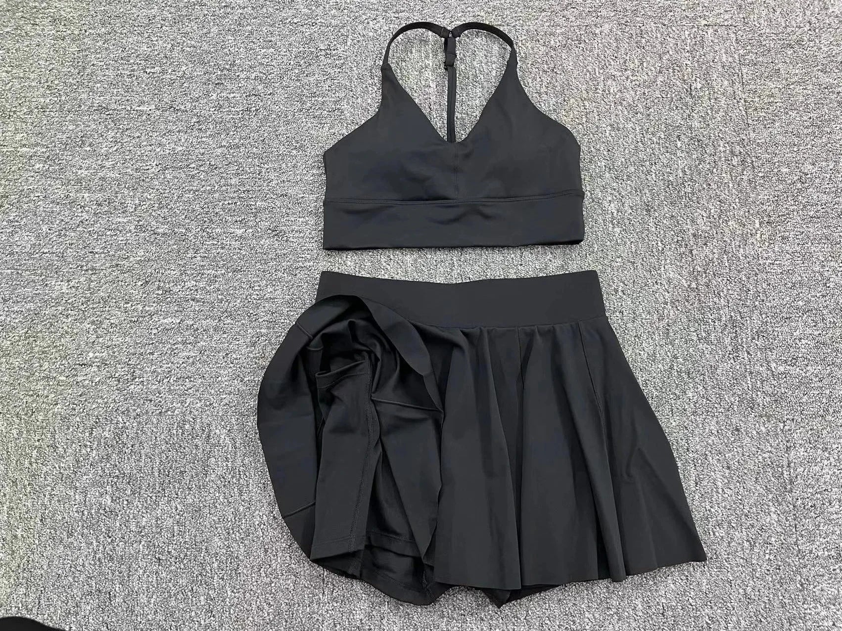 Black sports bra and skirt set on a textured gray surface