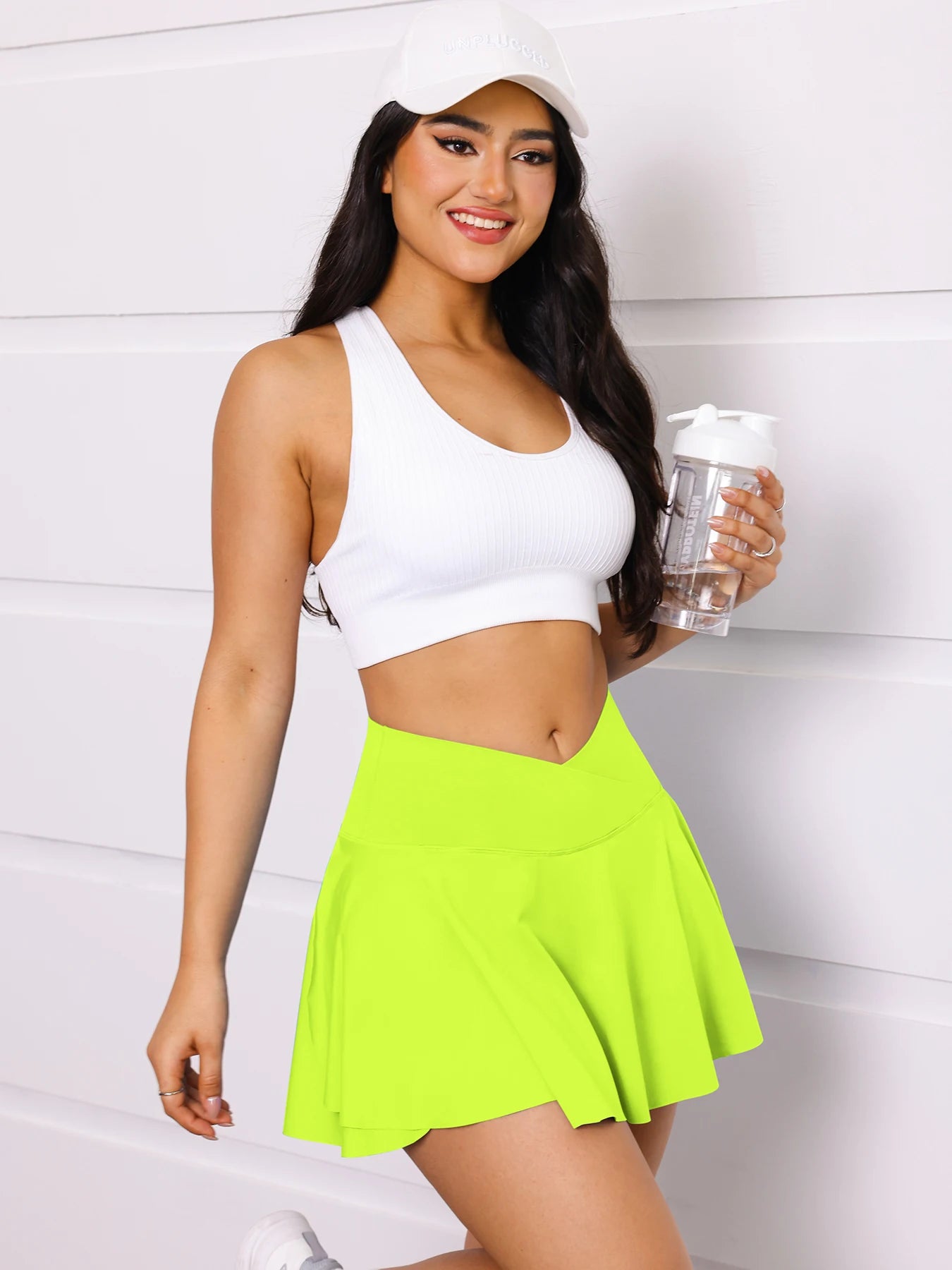 Woman in athletic wear holding a water bottle against a white background