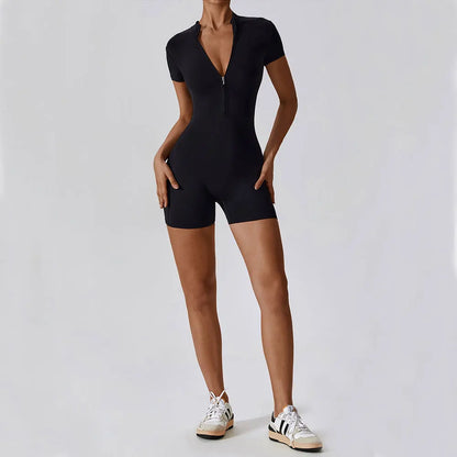 Person wearing a black romper with white sneakers on a light gray background