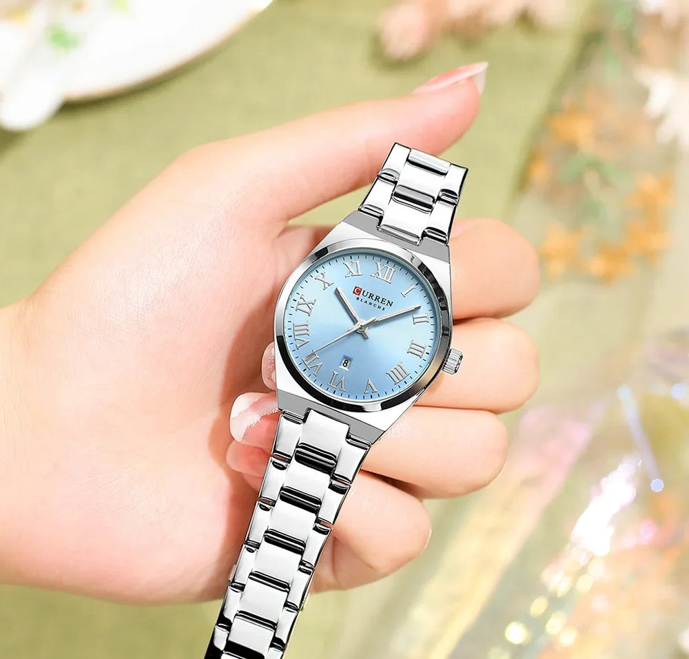 Silver watch with a blue face held in a hand against a blurred background