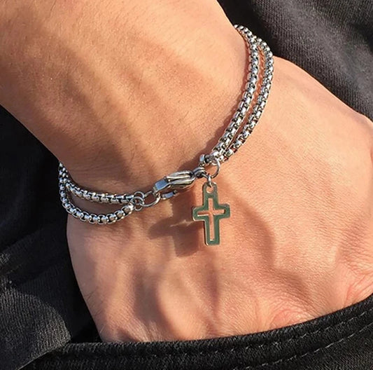 Close-up of a wrist wearing two silver bracelets with a cross charm.