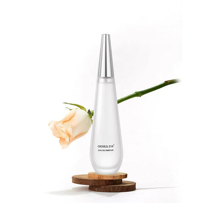 Clear perfume bottle with silver cap on a wooden coaster, white background