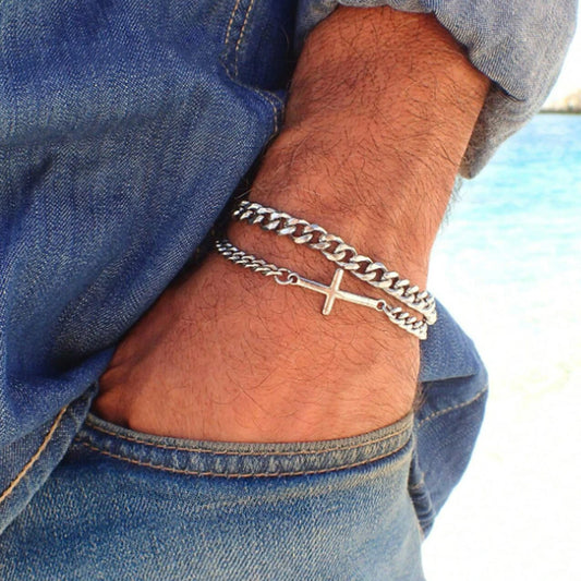 Silver chain bracelet with a cross pendant on a person's wrist, wearing blue jeans.